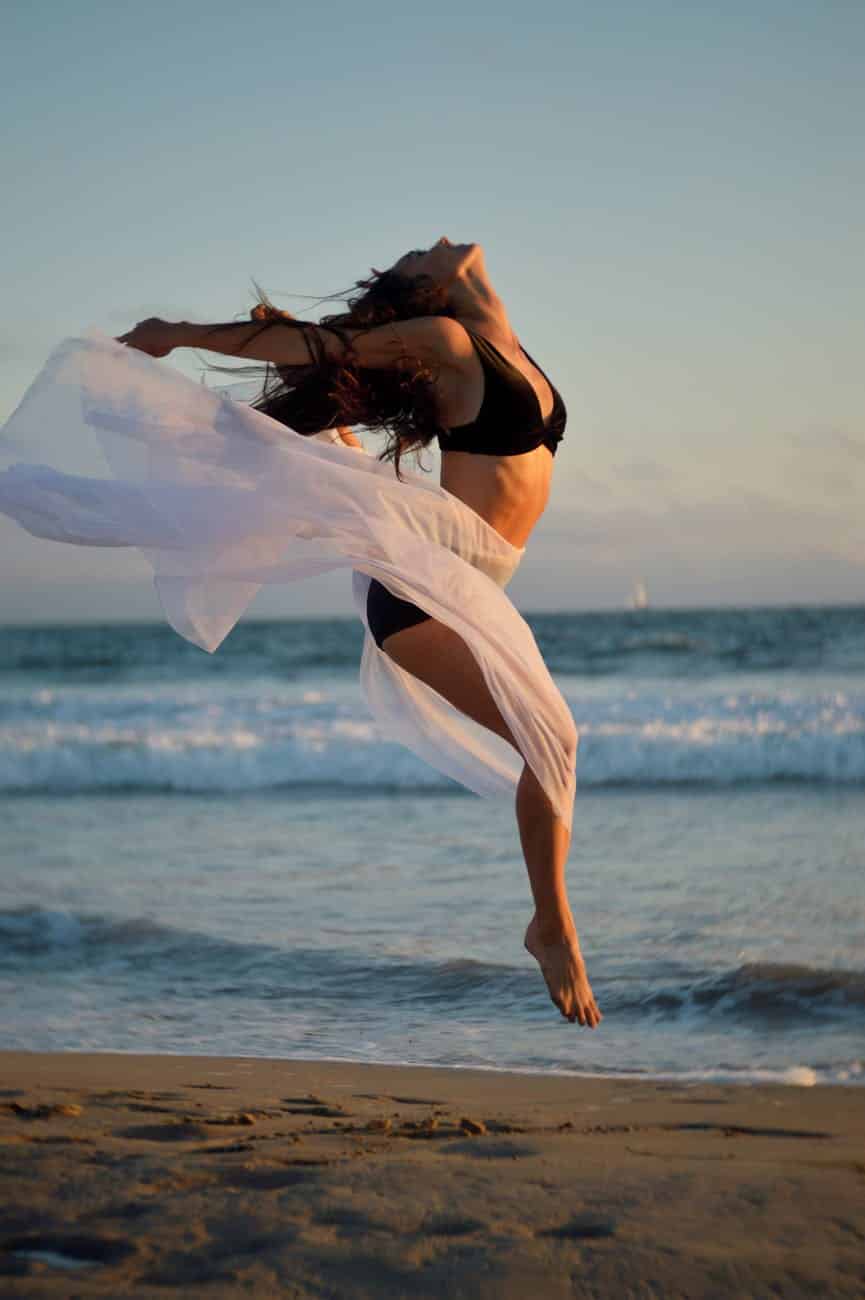 skinny dancer jumping over sandy shore of ocean