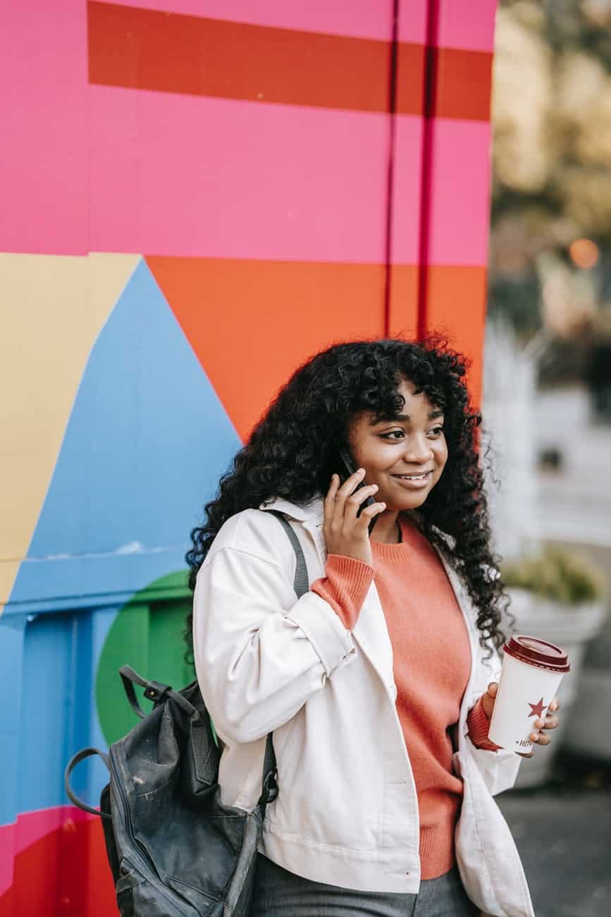 black woman with takeaway coffee talking on smartphone on street