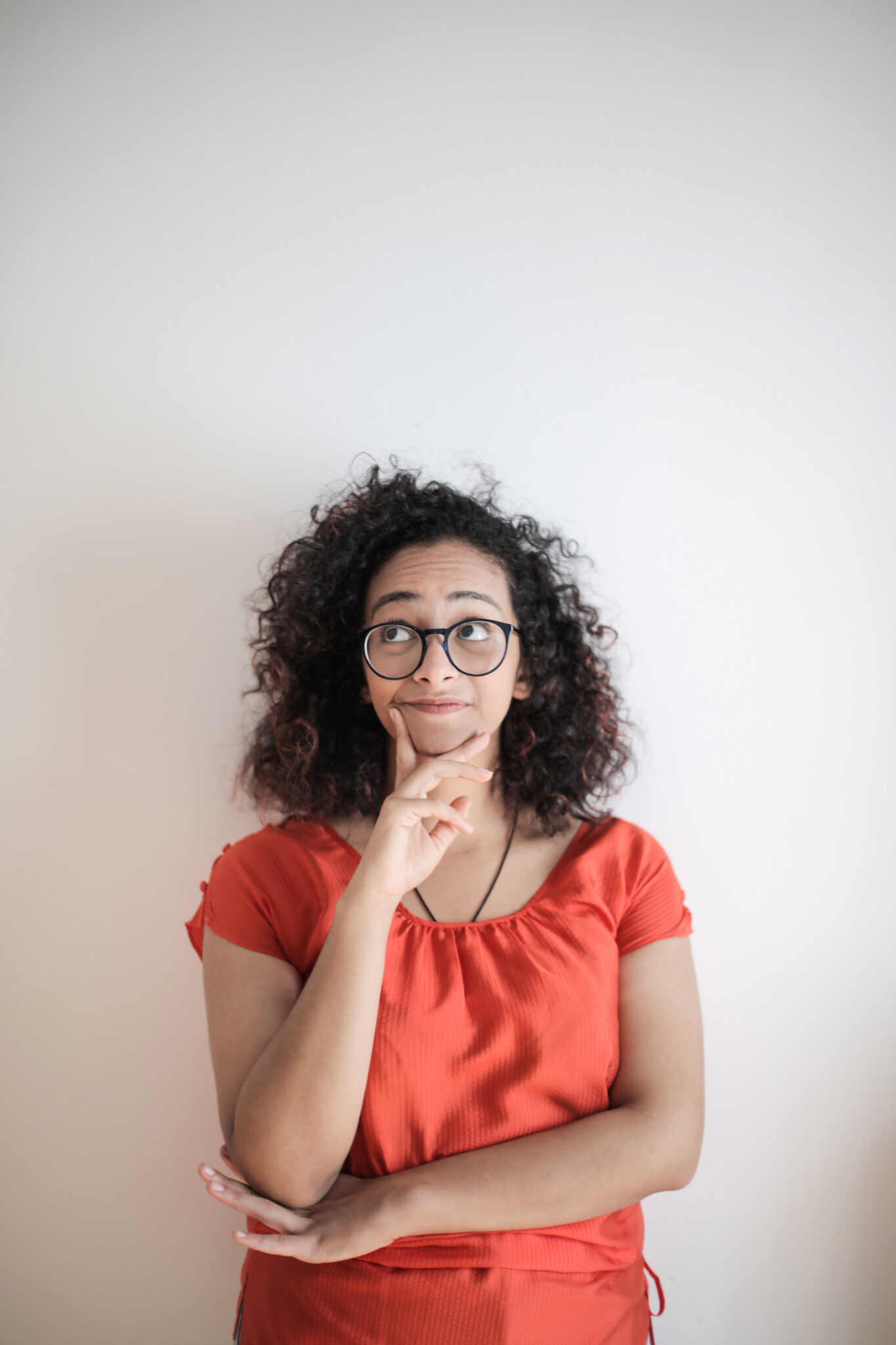 portrait-photo-of-woman-in-red-top-wearing-black-framed-eyeglasses-standing-in-front-of-white-background-thinking-stockpack-pexels