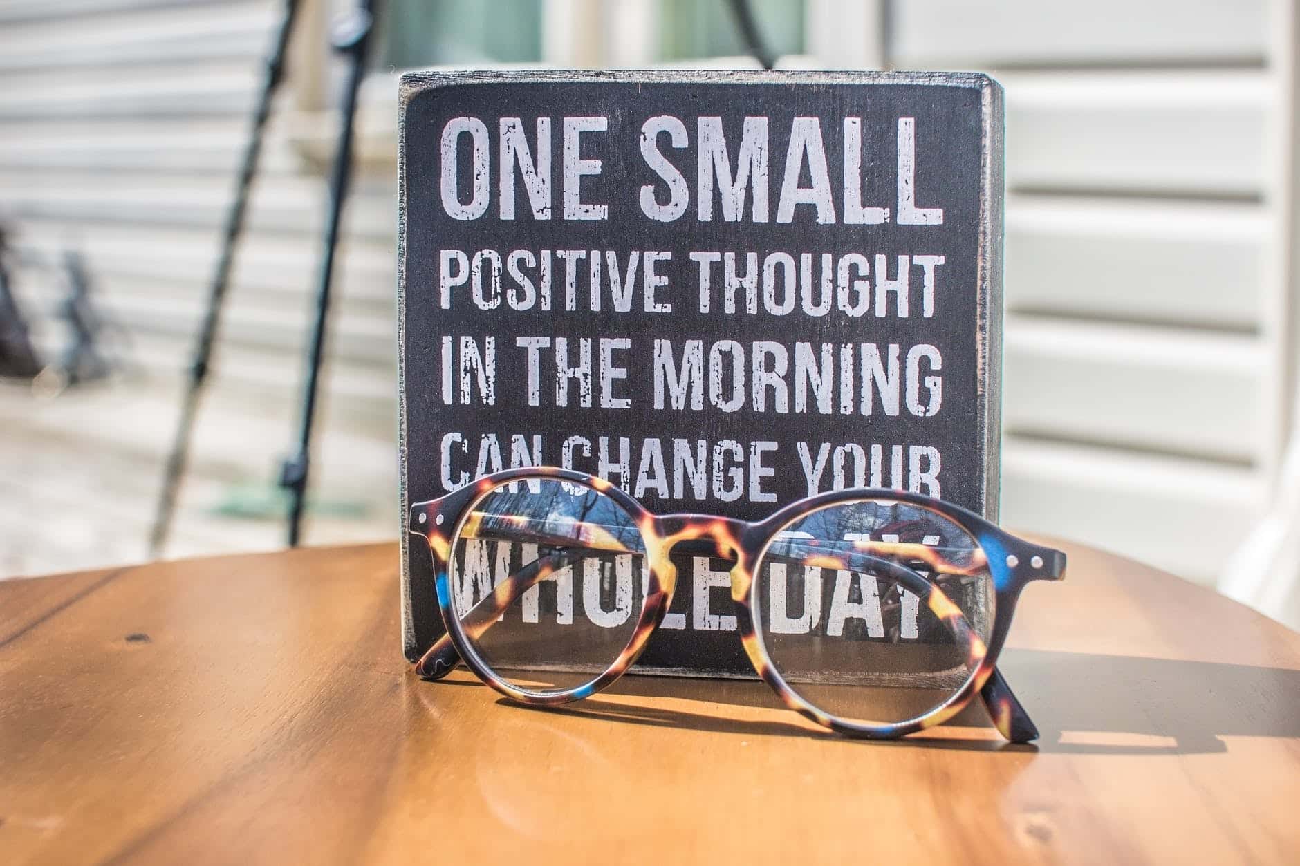 photo of a sign that reads one small positive thought in the morning can change your whole day, and eyeglasses on table