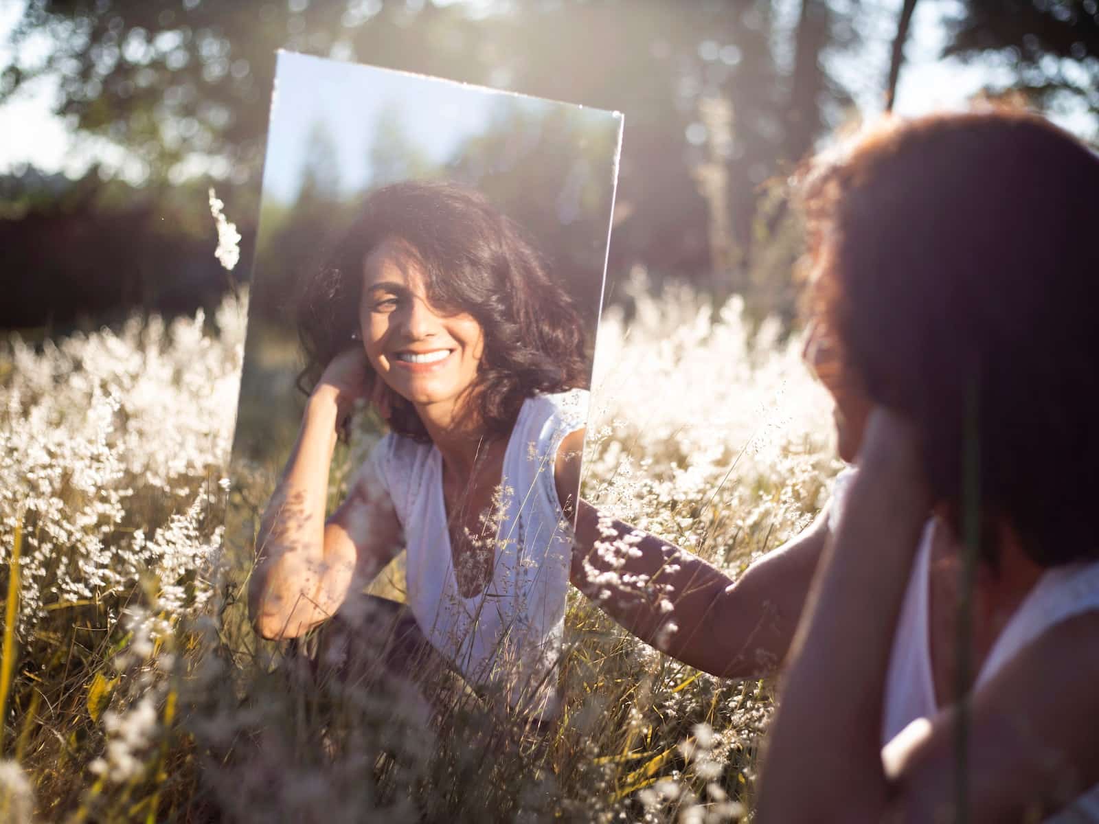 woman looking at herself in the mirror in a field of flowers